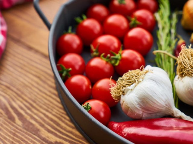 A vivid display of fresh Mediterranean vegetables on a wooden table with a pan.